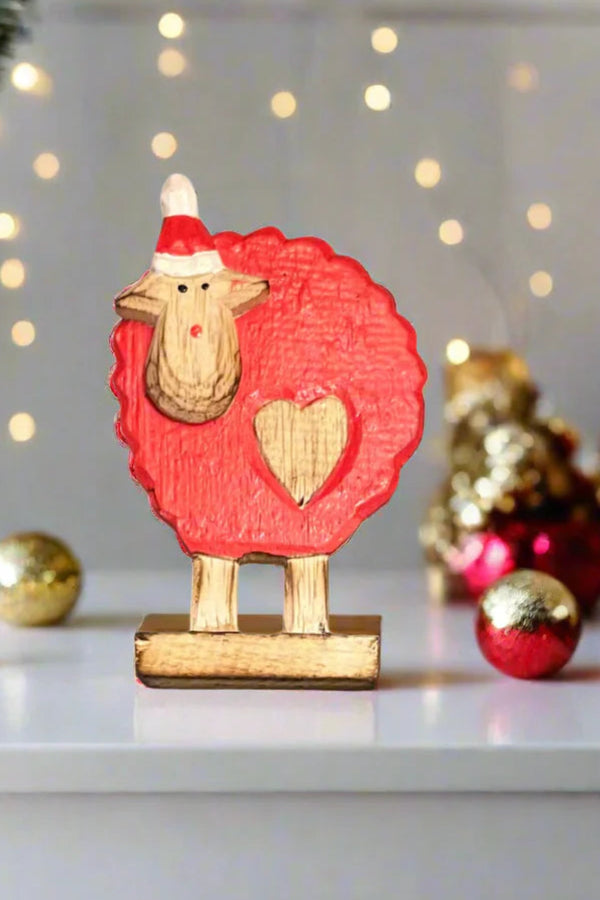 Decorative sheep figurine with a red coat and Santa hat on a white surface with Christmas decorations.