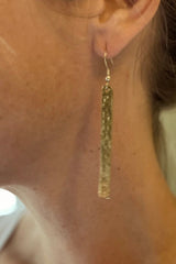 Gold tassel earring worn by a person with a neutral background