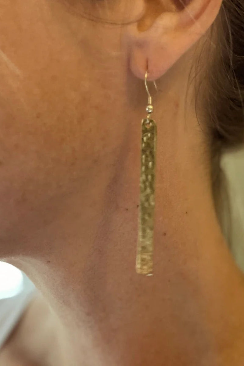 Gold tassel earring worn by a person with a neutral background